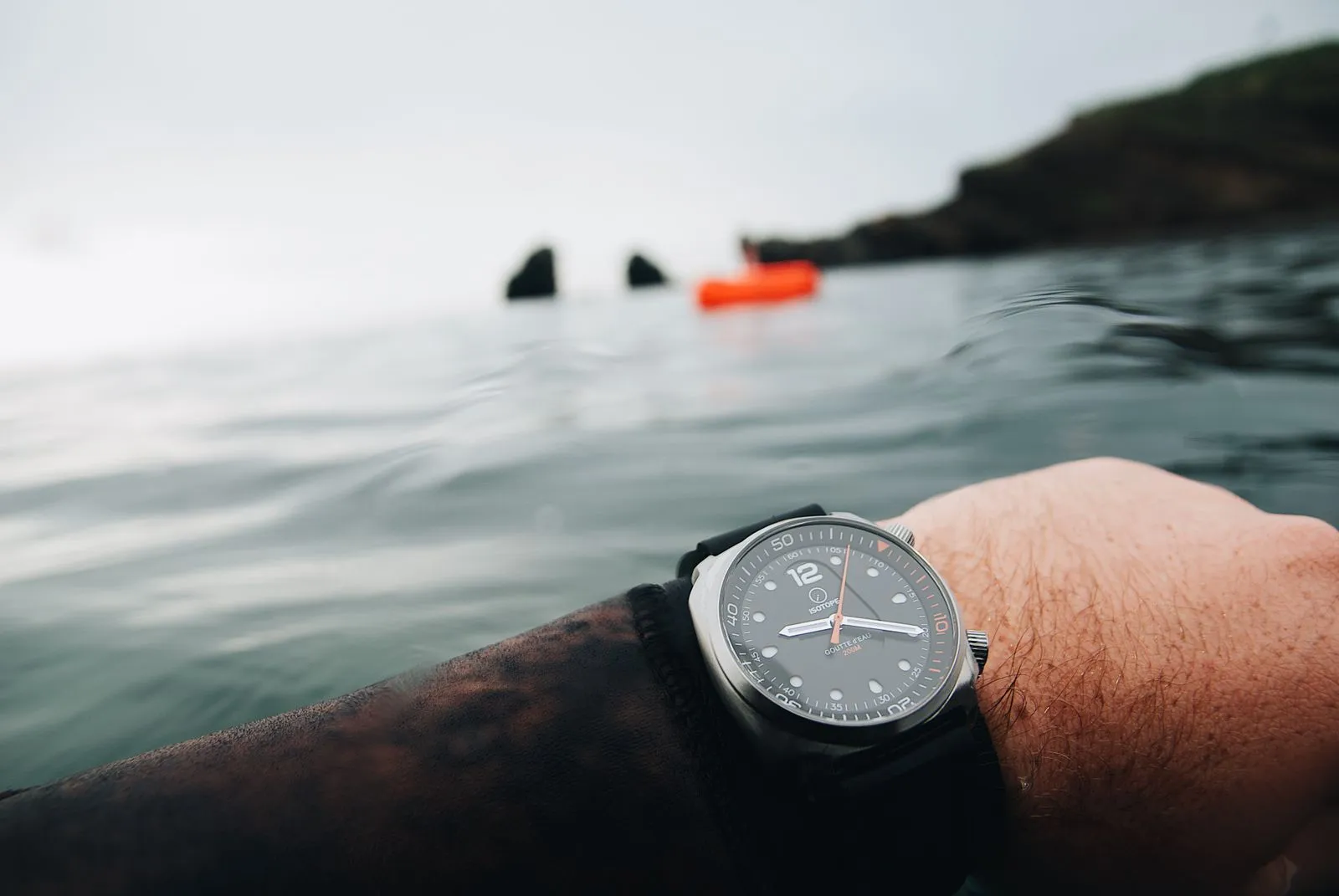 Une montre à cadran gris portée au poignet, au ras de la mer